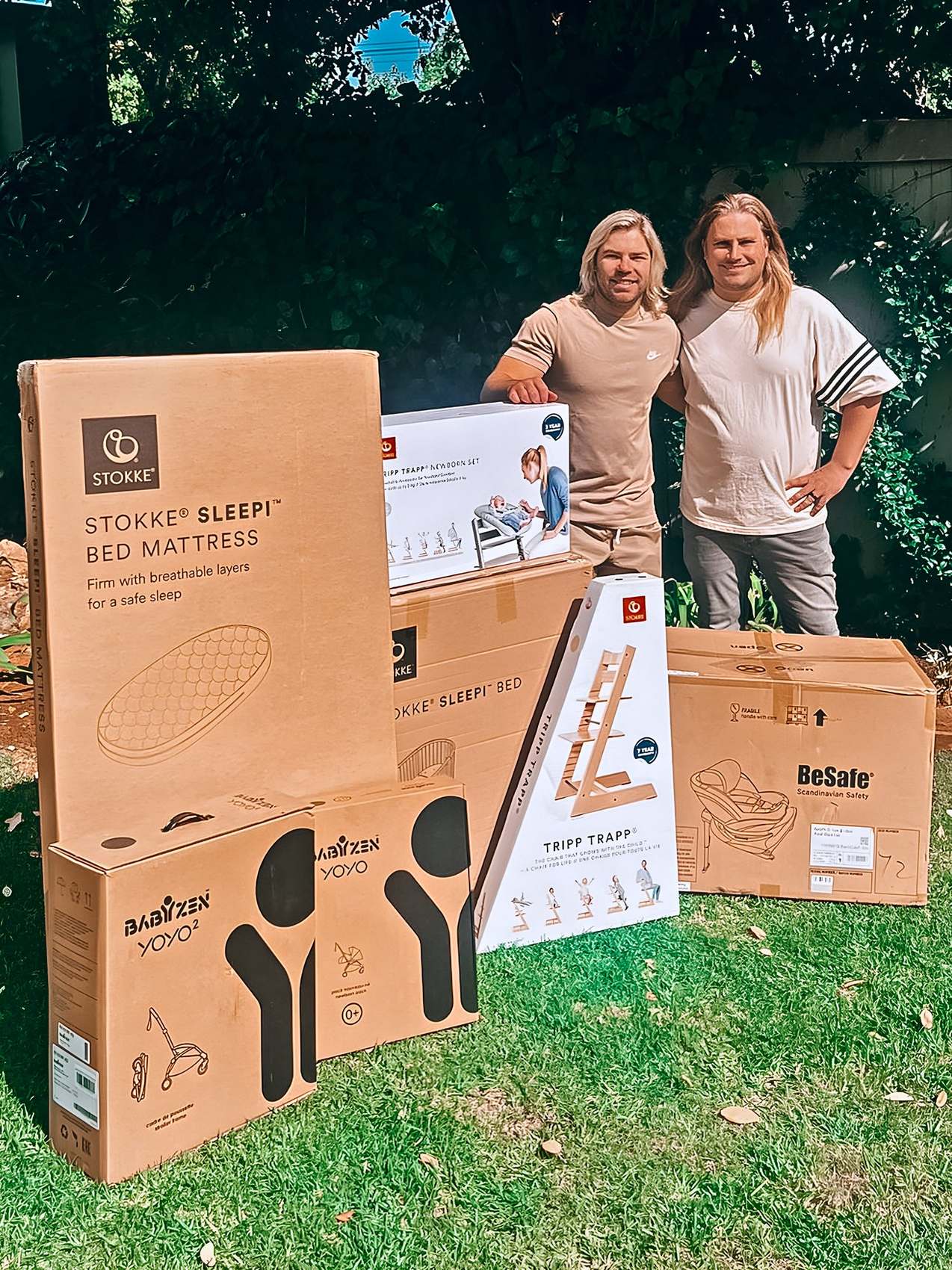 Faf de Klerk × Born Fabulous campaign: a couple standing behind boxed Stokke baby furniture on a garden lawn