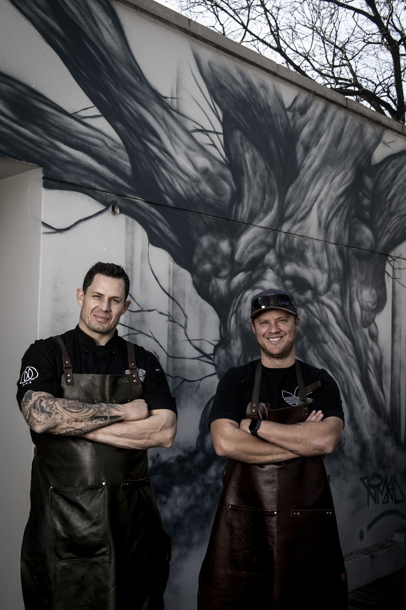 Double Dutch: Two chefs in aprons in front of a tree mural