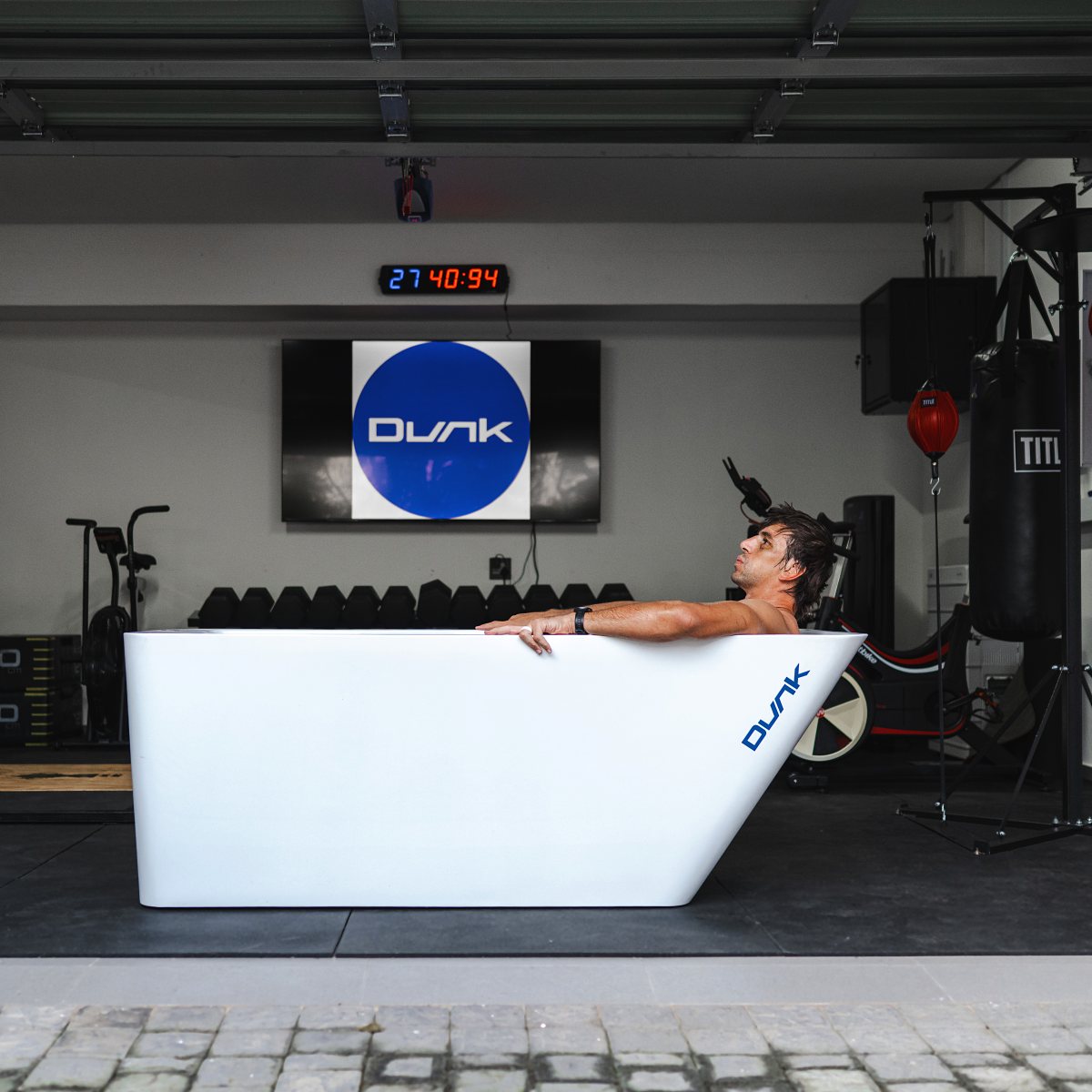Man in a white Dunk ice bath in a home gym with the Dunk logo on screen