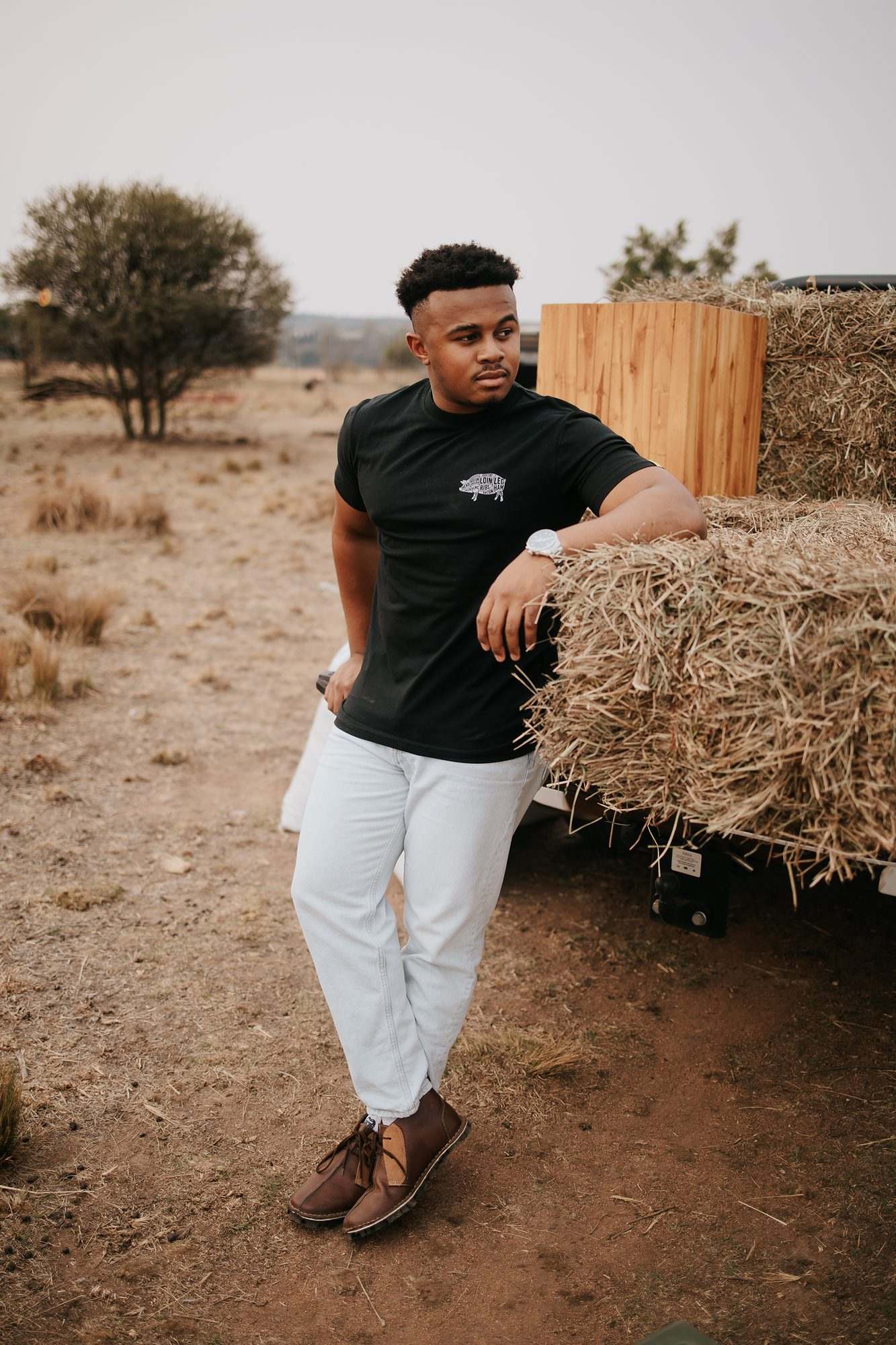 Mieliestronk apparel shoot: model in a black Mieliestronk tee leaning on hay bales