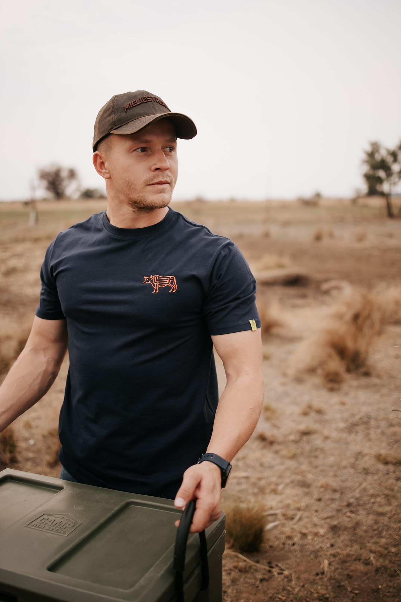 Mieliestronk: Man in a navy tee and cap carrying a feed bin on a farm