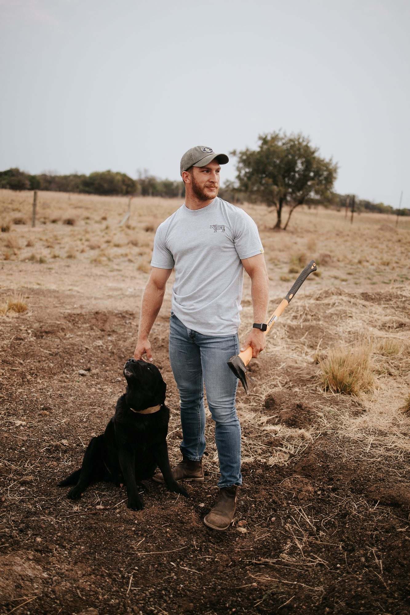 Mieliestronk: Man in a grey tee standing with a black dog on the farm