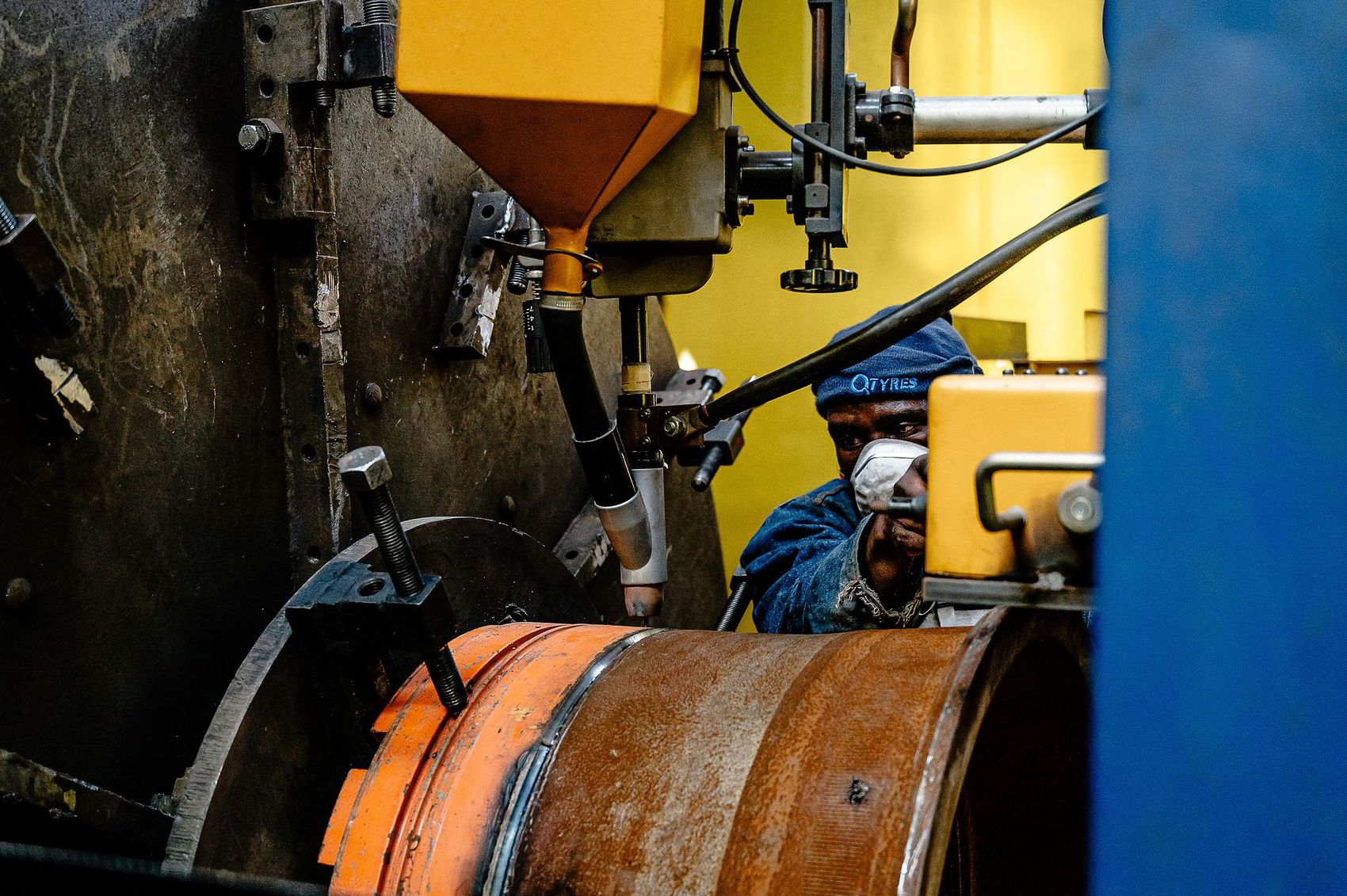 Q Tyres: Masked worker at a machine refurbishing an orange wheel rim