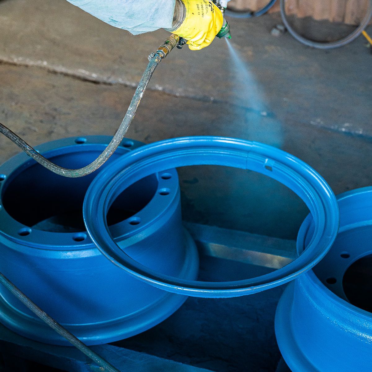 Q Tyres rim refurbishing: hand spray-painting blue wheel rims in the workshop