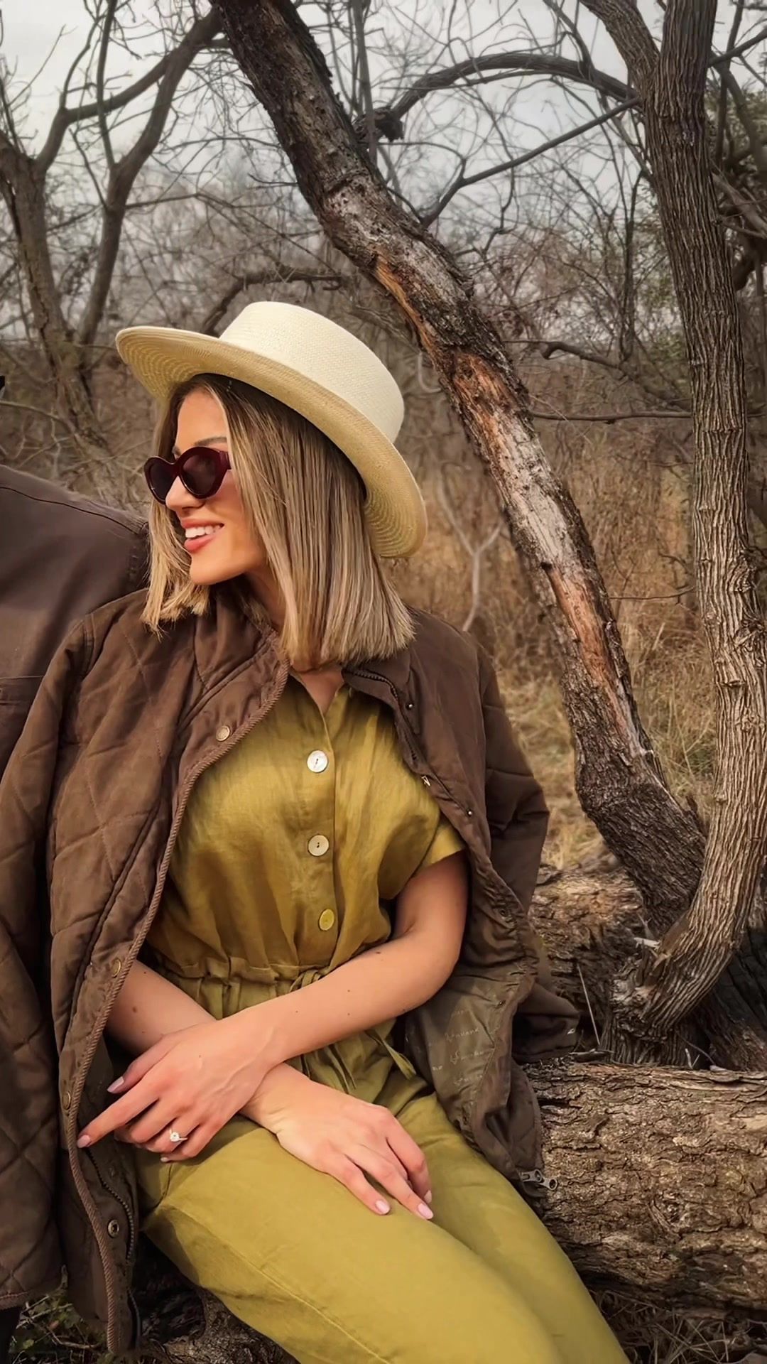 Safari Outdoor lifestyle shoot: woman in a wide-brim hat and olive outfit seated on a log in the bushveld